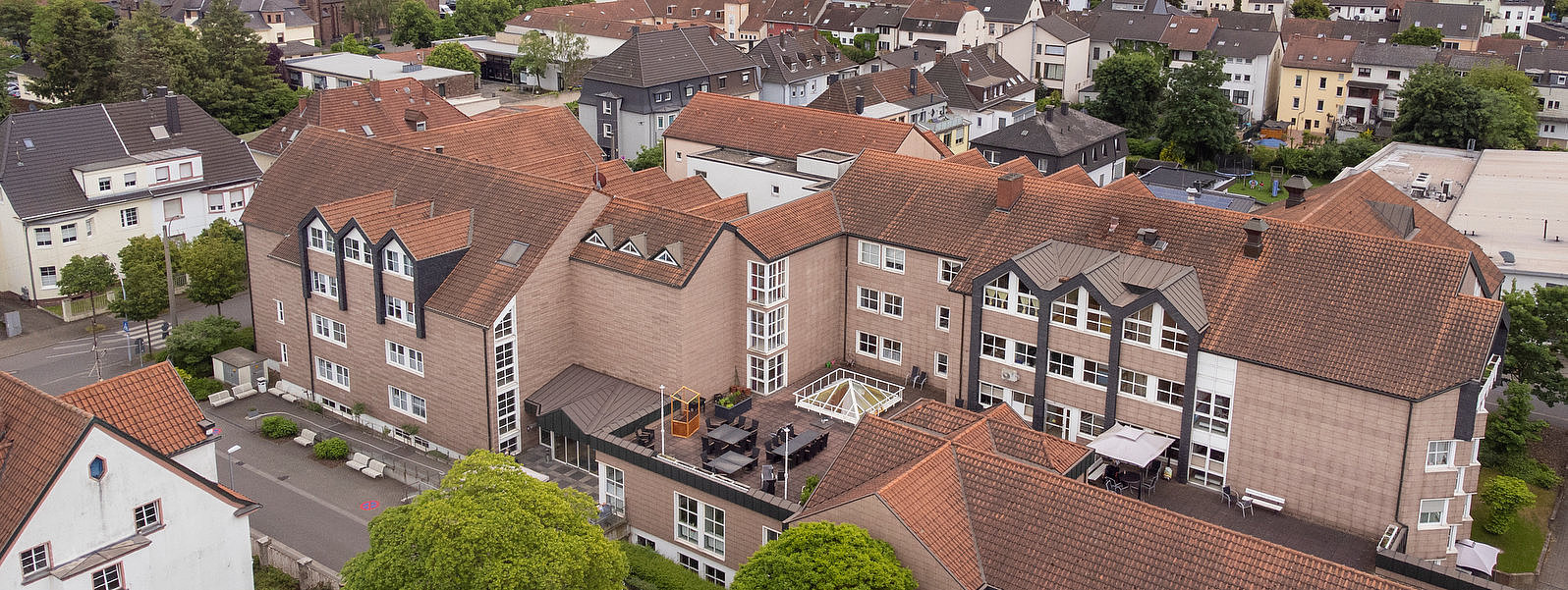 Luftaufnahme eines Wohngebiets mit roten Ziegeldächern und einer Stadt mit Industrieanlagen im Hintergrund